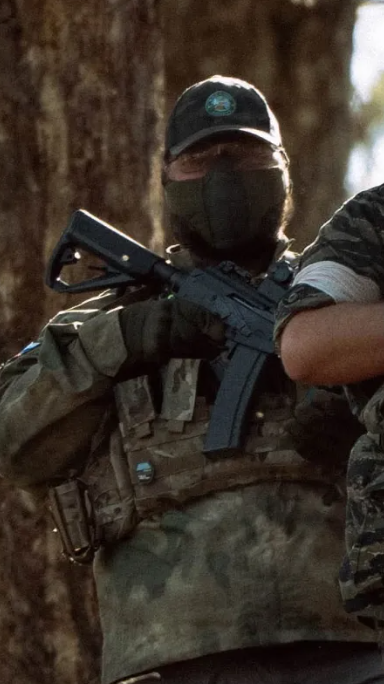 Trenton of Mike Force Irregulars in camo and face mask holding a rifle in a forested airsoft field